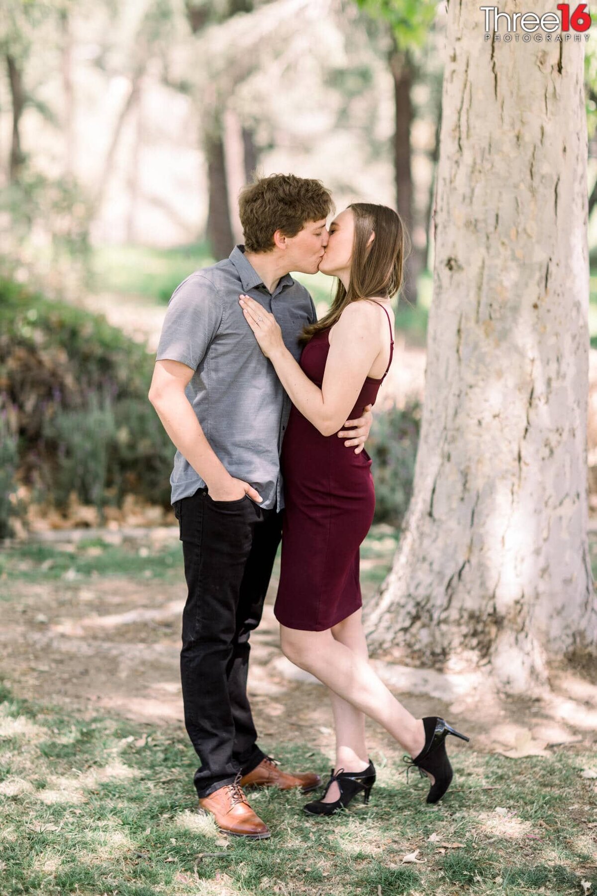 Engaged couple share a romantic kiss under a tree