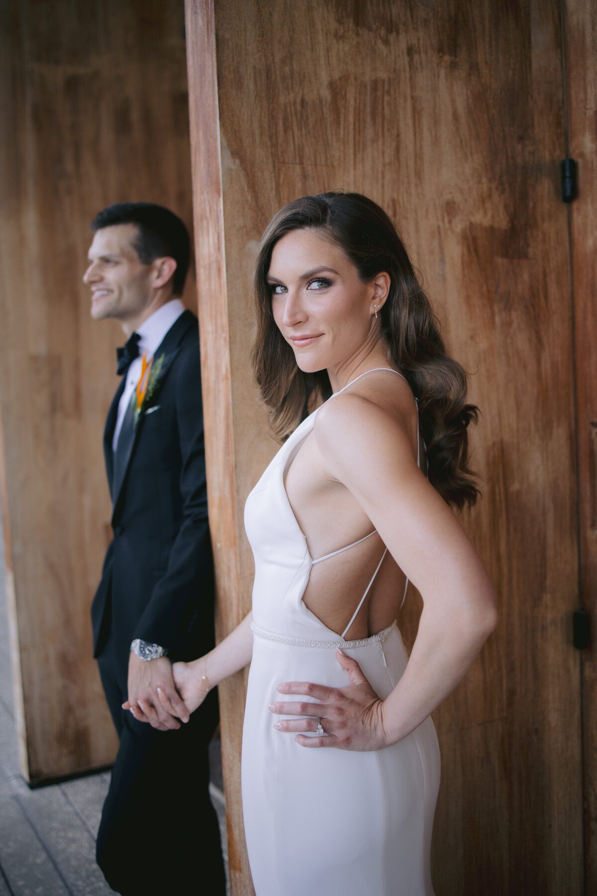 Bride and groom holding hands against a rustic wooden backdrop, captured by Rodrigo Varela Photography.