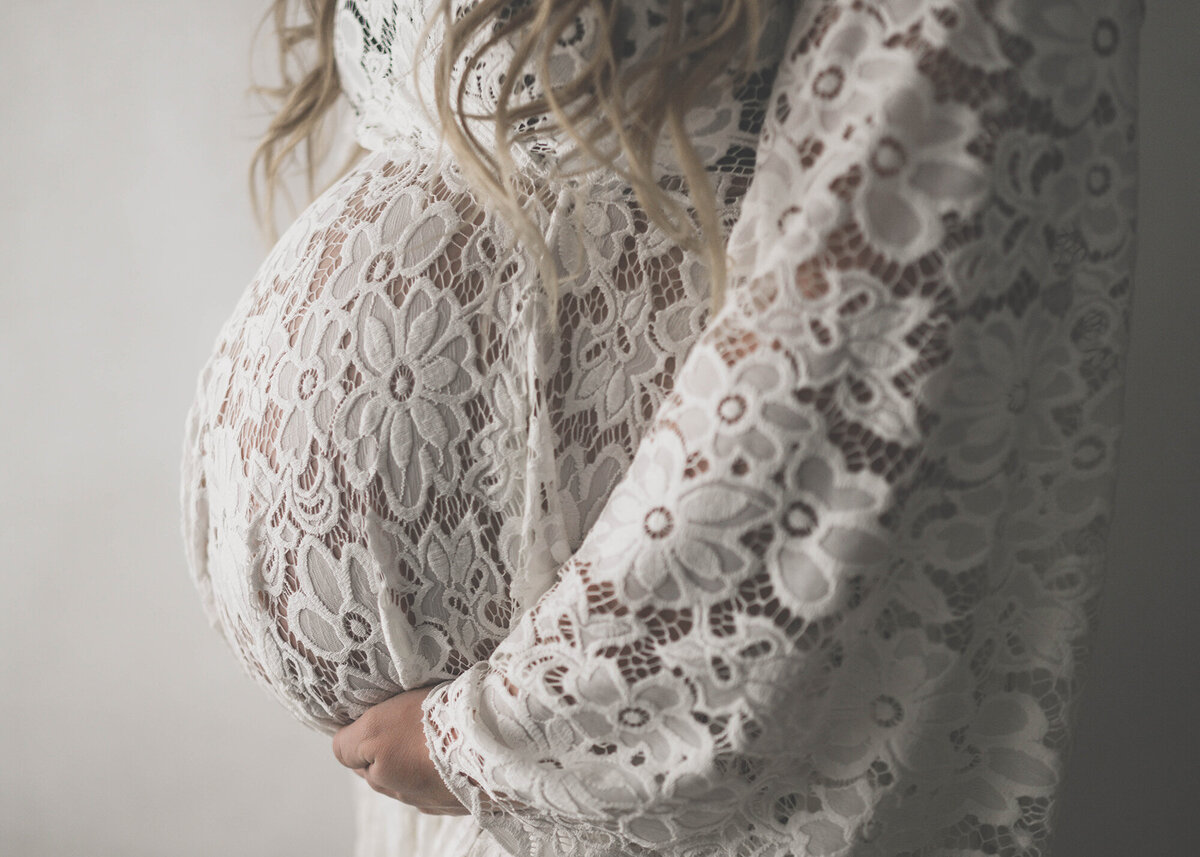 A profile image of a pregnancy bump in a white lace maternity gown