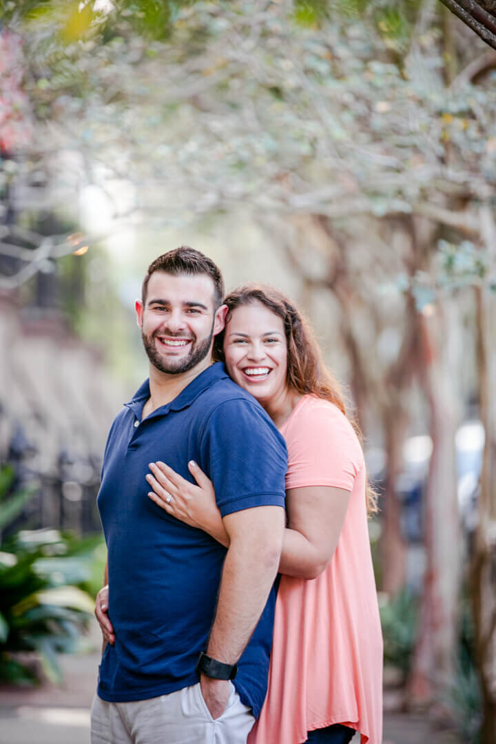 A couple embrace while standing on a sidewalk in Savannah, GA.