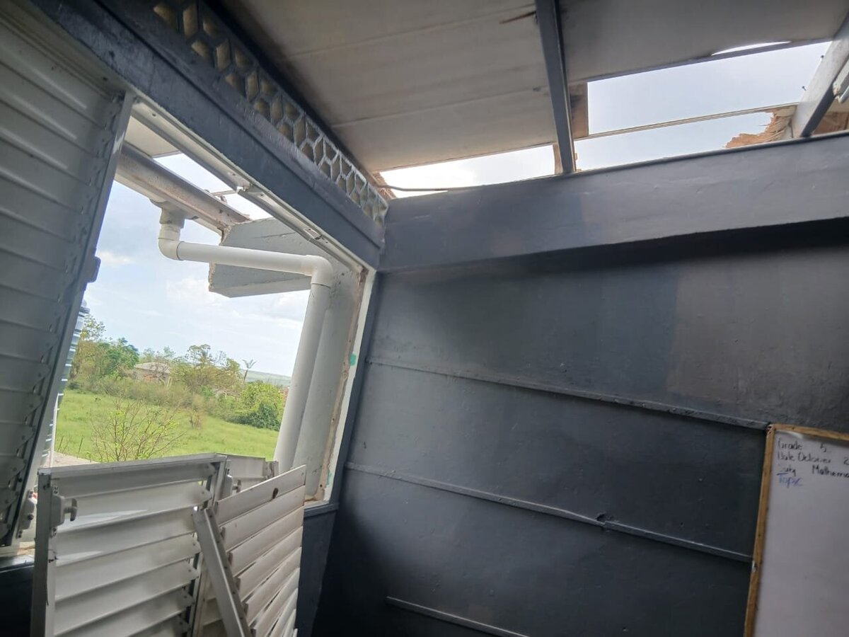 Interior wall damage with exposed metal and broken roof sections inside the school.