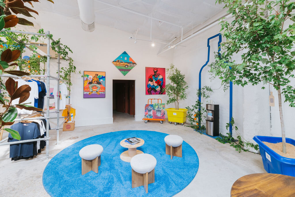 Gallery lounge with Absolut Vodka art, blue rug seating area, and indoor plants at the Like Minded Creatures installation.