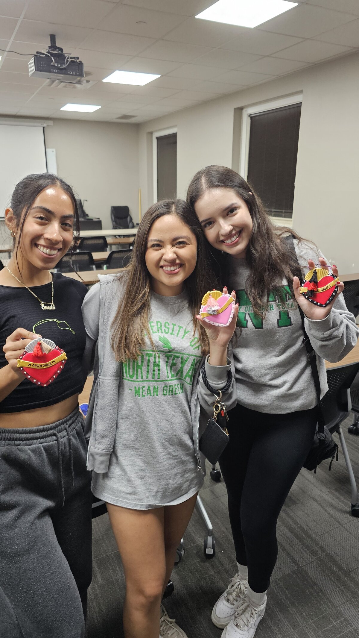 The warmth of friendship as three girls hug each other, proudly showcasing the vibrant graphic pieces they crafted in a workshop at Soleil Vida Studio. Dressed in cozy gray sweatshirts, they've brought to life colorful hearts adorned with inspirational phrases