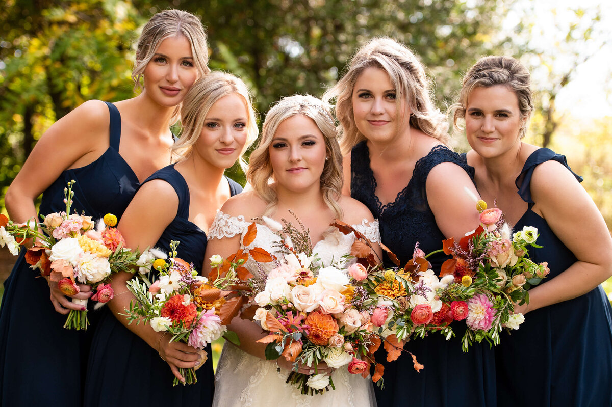 a group photo of a fall bride with her bridesmaids wearing navy gowns and holding fall coloured bouquets.  Captured by Ottawa wedding photographer JEMMAN Photography