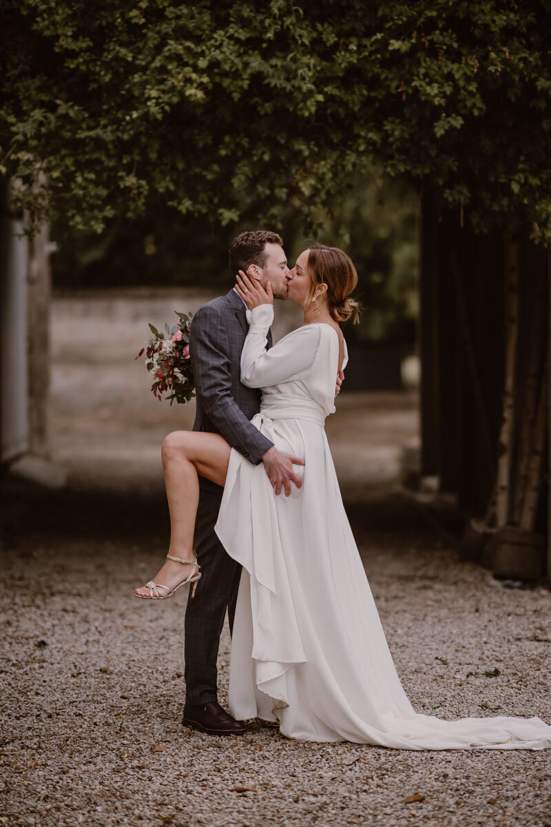 Couple de mariés qui s’embrassent avec fougue dans une allée en Provence, moment intense et passionné.