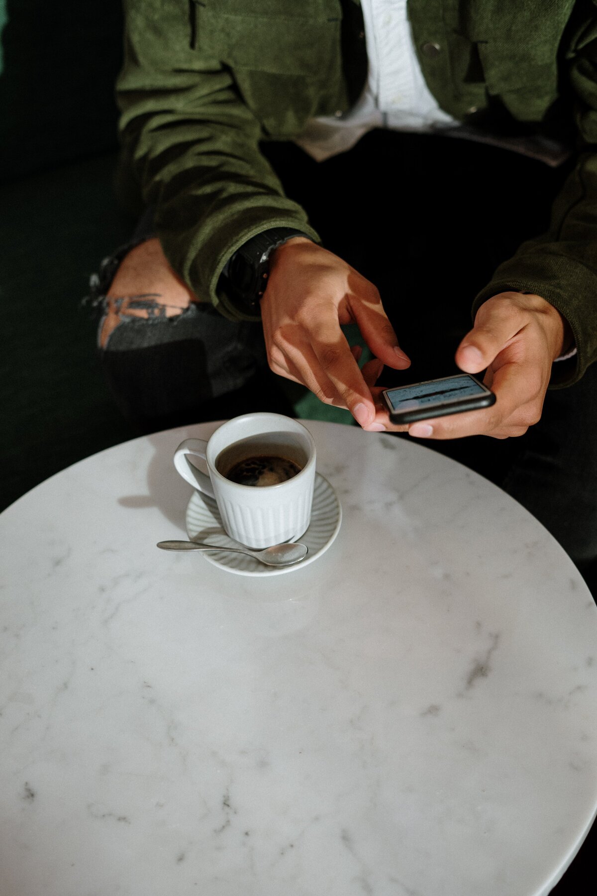 man on his phone next to coffee on a table