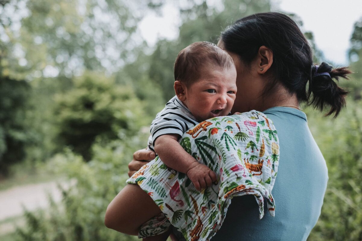 Mother holds small baby who is alert and looking out, leaning on a colorful muslin cloth