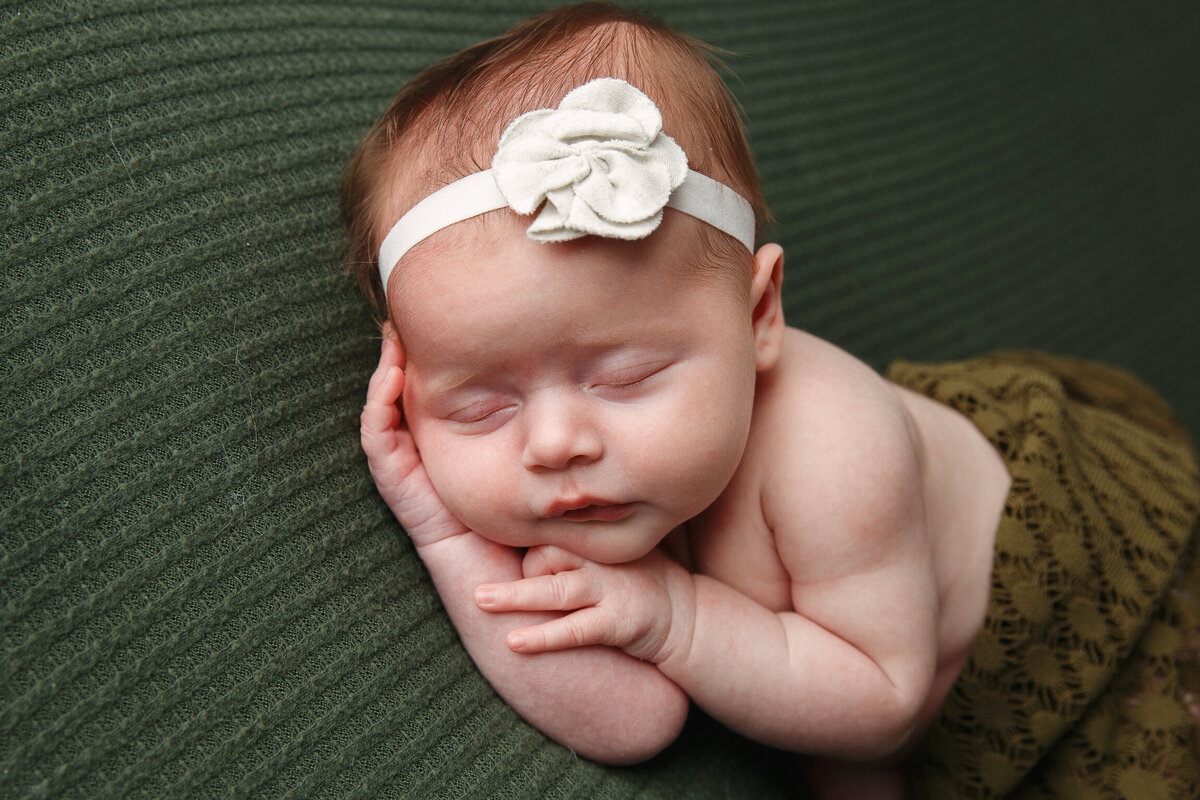 Beautiful portrait of a baby girl wearing a white headband and sleeping on a green rug