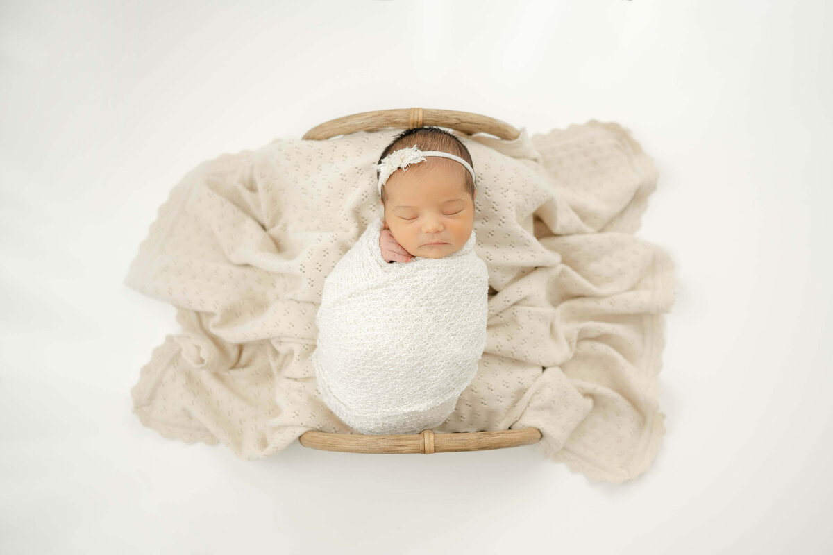 newborn baby girl sleeping in a tiny bed in a all white oklahoma city photography studio