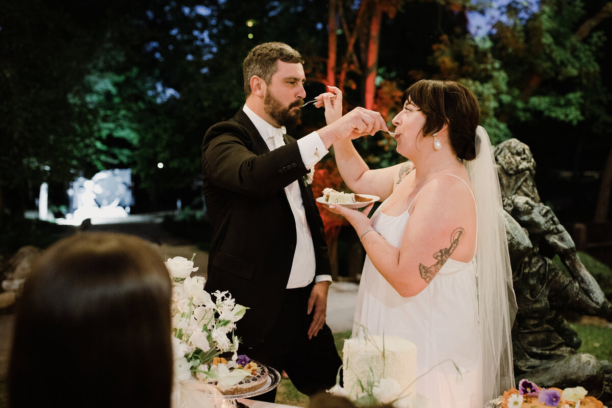 Bride and groom feeding cake to each other at Umlauf Sculpture Garden, Austin