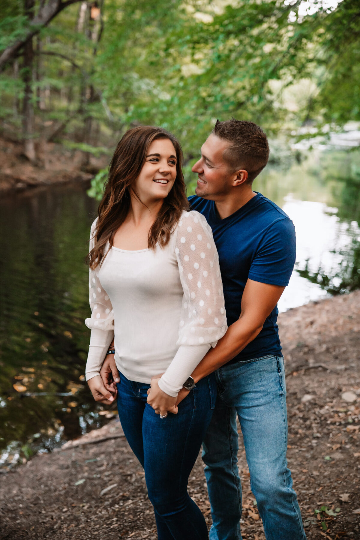 man holds womans hips while smiling at each other in front of river in West Bend