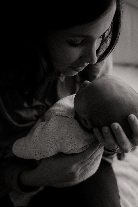 Maman regardant son bébé qu'elle tient dans ses bras pour une séance photo naissance. Photo en noir et blanc.