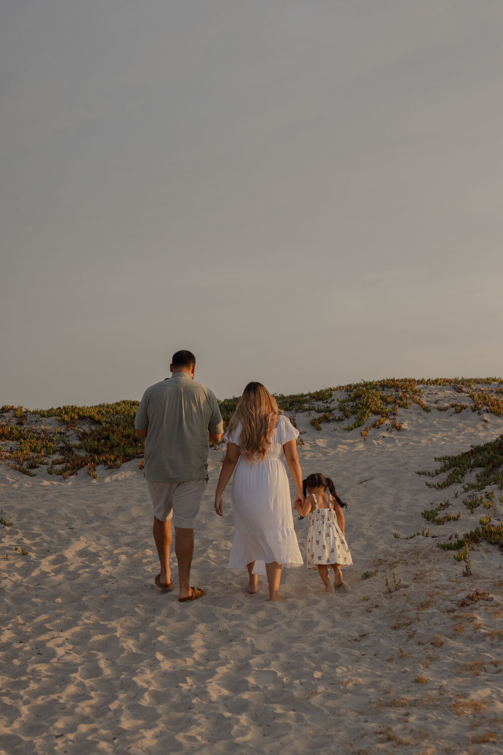 Family walking up a sandy path from the beach, holding hands during a sunset session