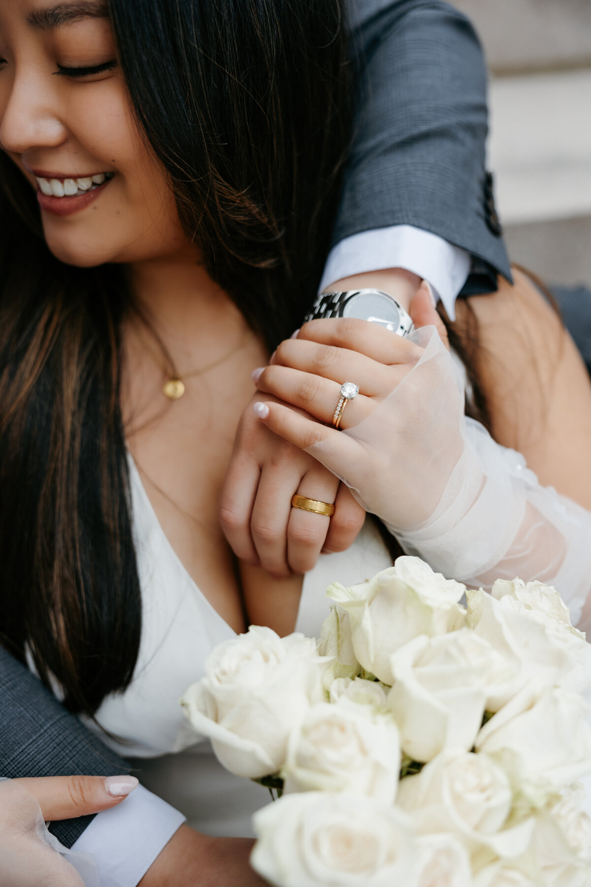 Close up image of bride and groom's hands on top of each other's showing their wedding rings and the bride's white rose bouquet