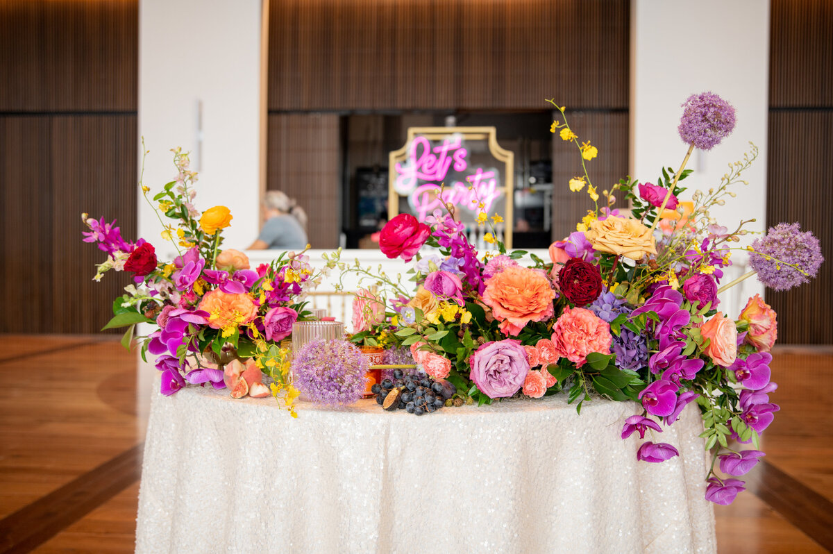 Artful sweetheart table arrangement composed orchids, roses, garden roses, allium, and ranunculus in hues of pink, fuchsia, orange, coral, golden-yellow, and lavender. Design by Rosemary and Finch in Nashville, TN.