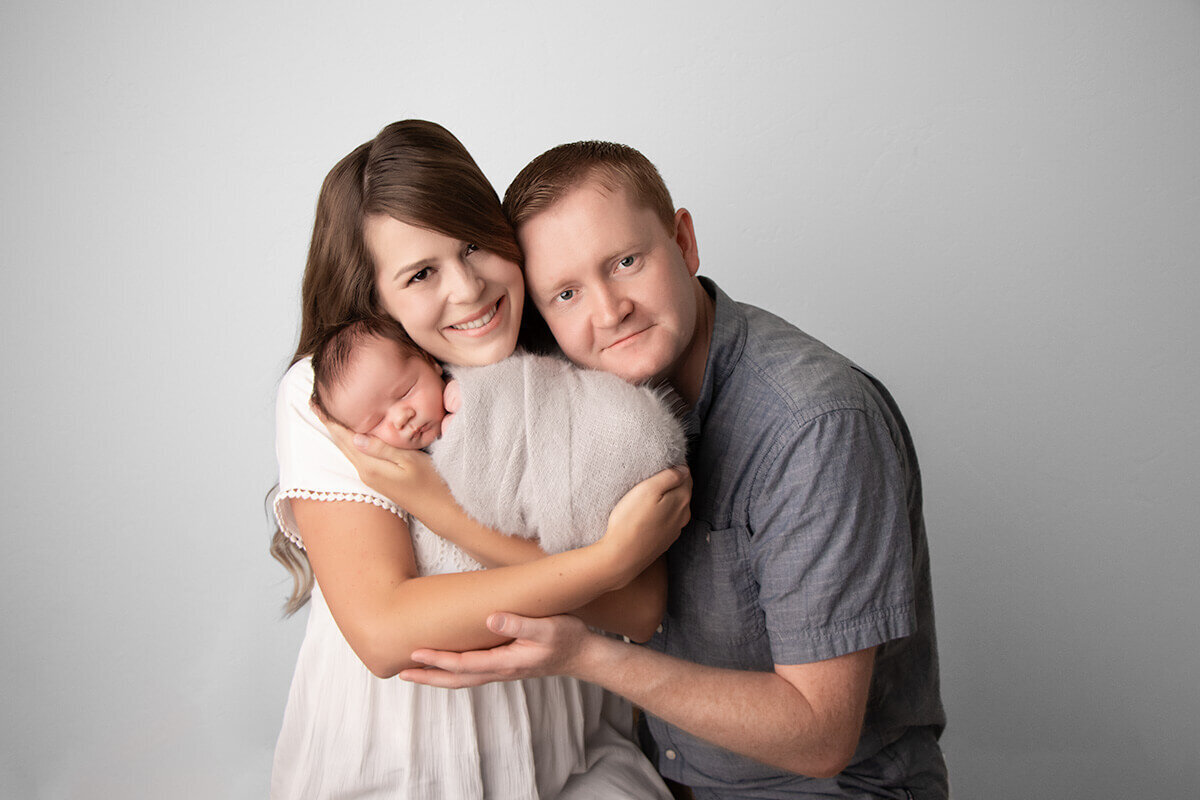 mother and father holding their swaddled newborn baby