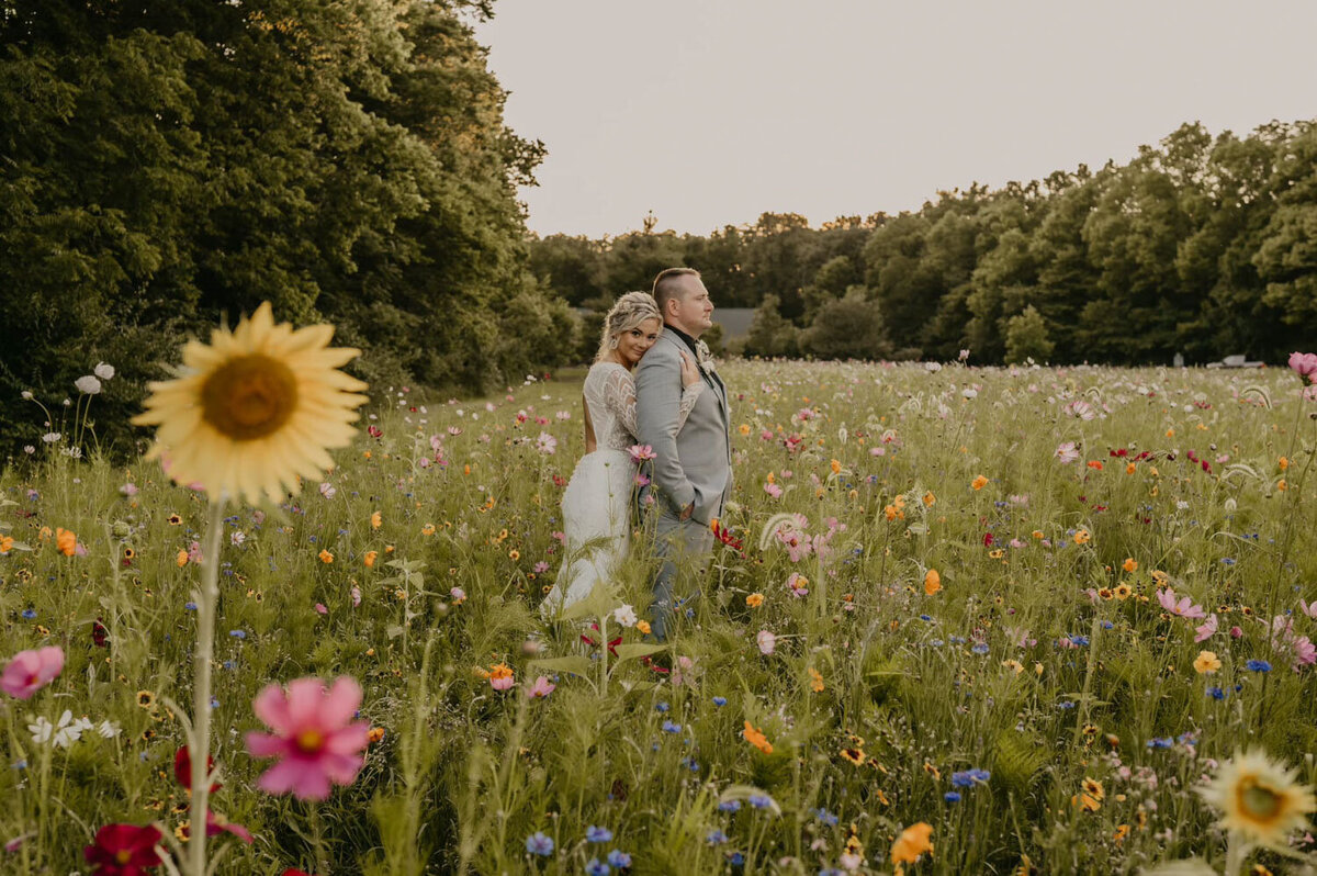 Bride and groom standing back-to-back in wildflower field