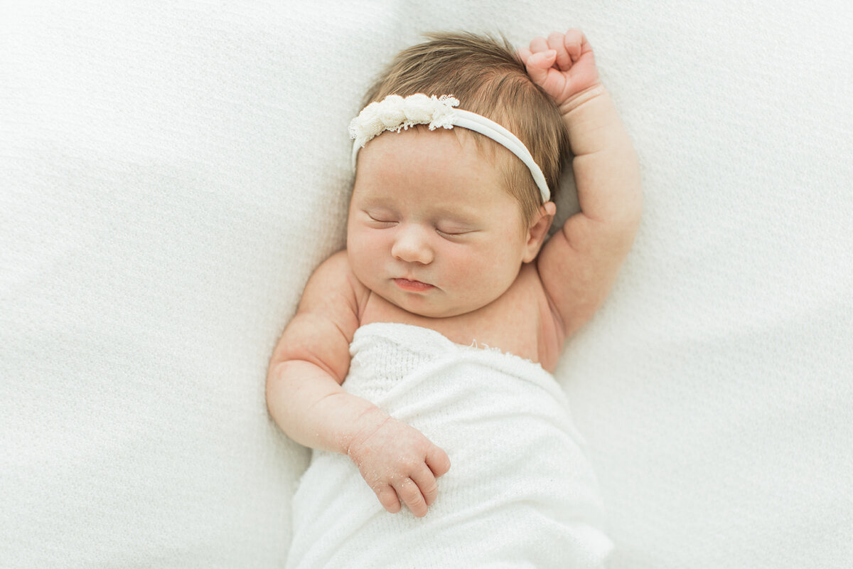 squishy newborn baby girls in a headband sleeps with one arm stretched above her head