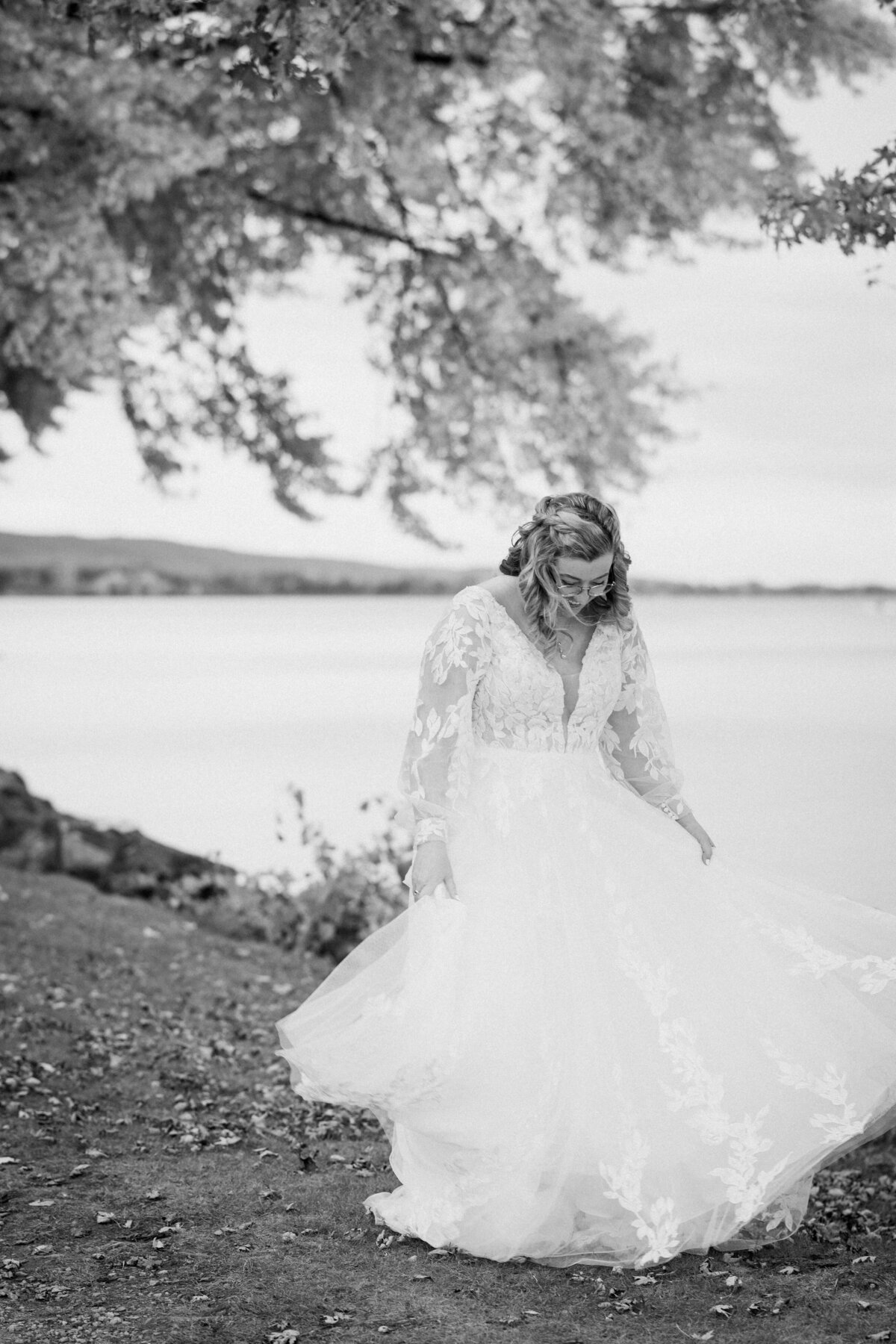 Bride smiles as she admires her wedding dress for her solo portrait by the lake