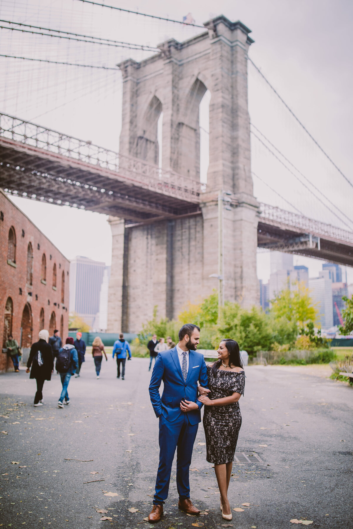 A couple walking down the pathway at brooklyn bridge park with the bridge in the background during their engagement session