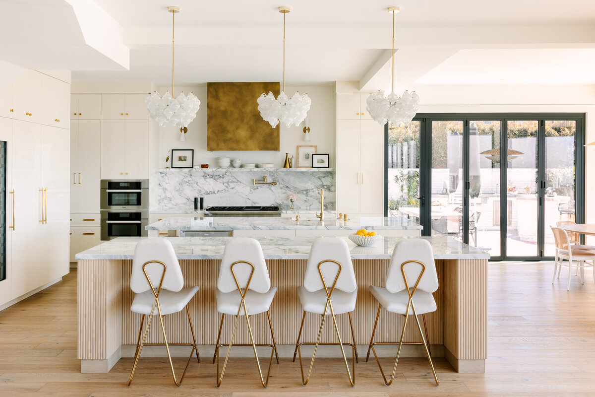 Kitchen with high gloss cream cabinets and Vagli marble counter and backsplash, brass range hood, Thermador appliances and vintage 1960's pendants.
