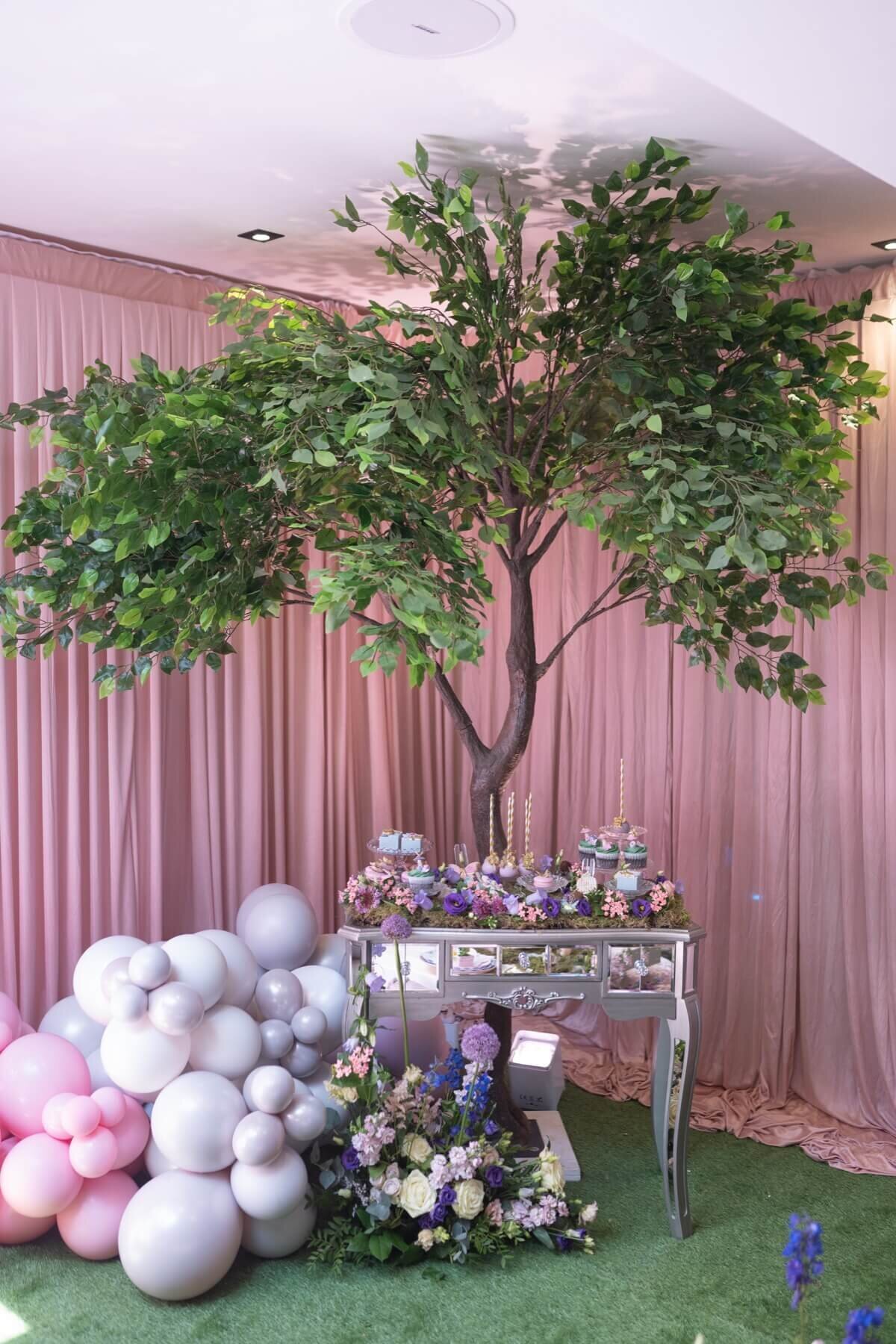 Garden theme kids sweet table on a vintage mirror table under a beautiful tree with flowers and balloon decoration