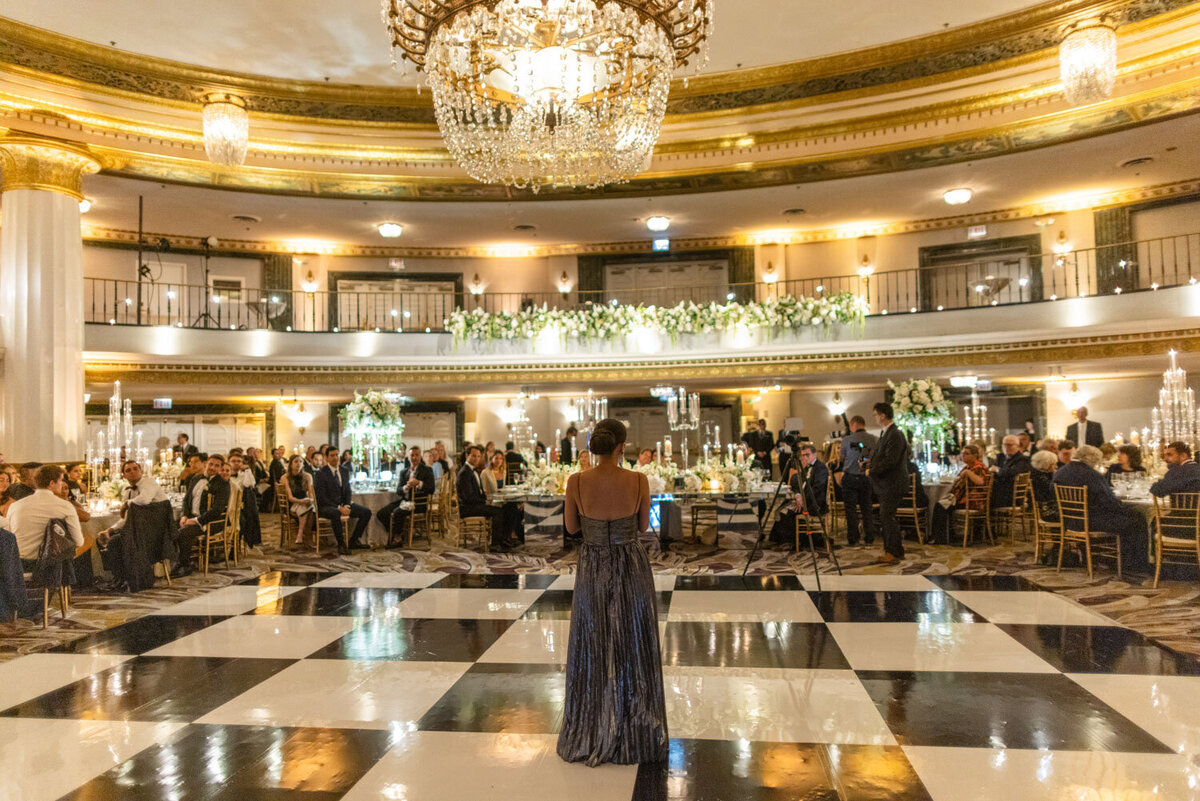 A woman in a long dress is standing on a checkered floor in a large room.