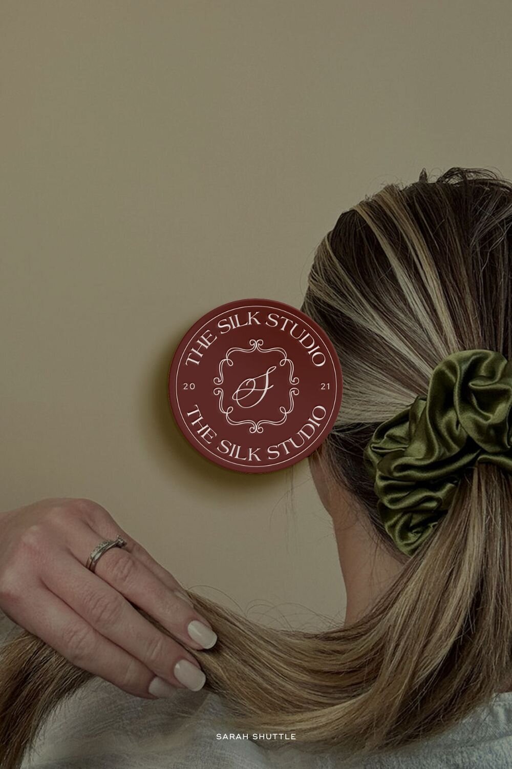 Submark in red over portrait of woman wearing a silk scrunchie — showing product-in-use styling