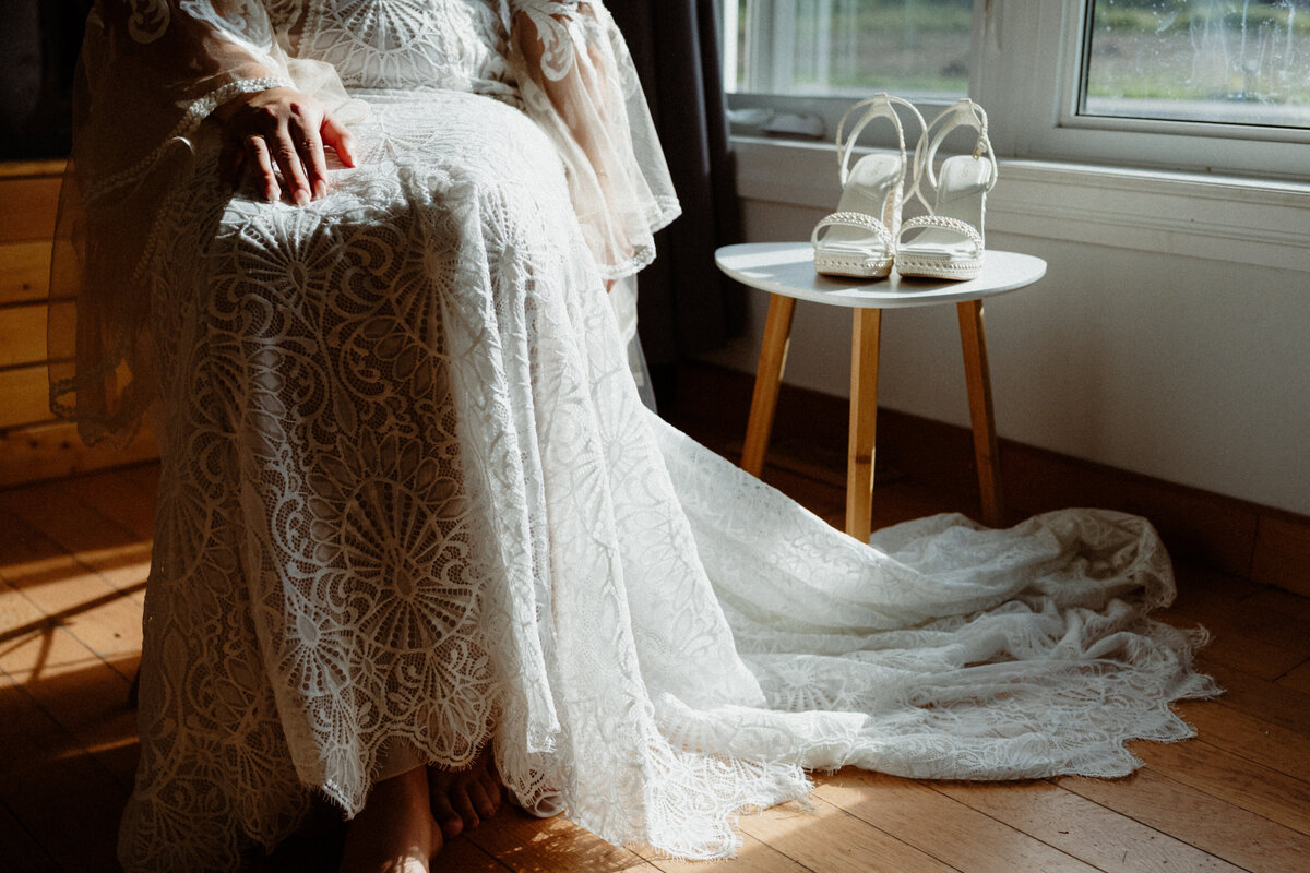close-up-of-a-sitting-bride-in-her-boho-dress-and-her-shoes-beside-her-1