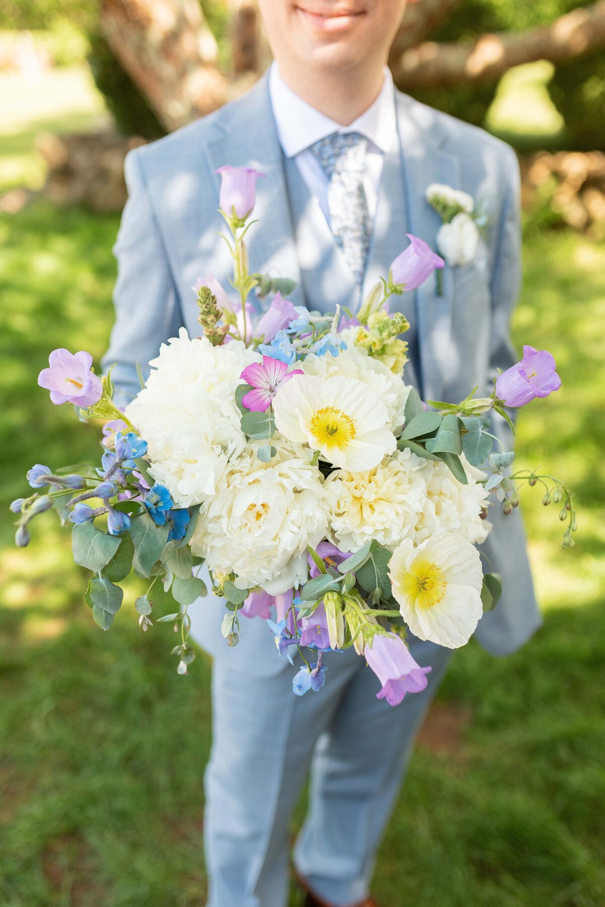 A groom in a light blue suit holds the bouquet.