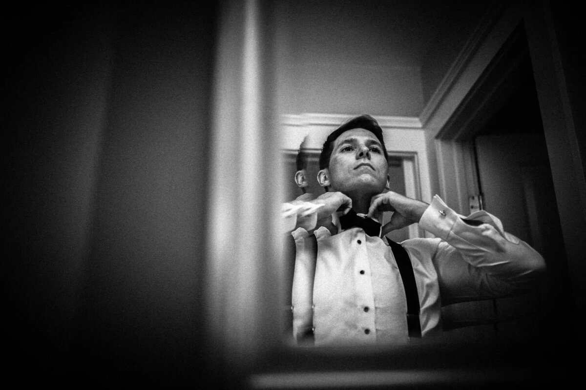 the reflection of a groom adjusting his bow tie.