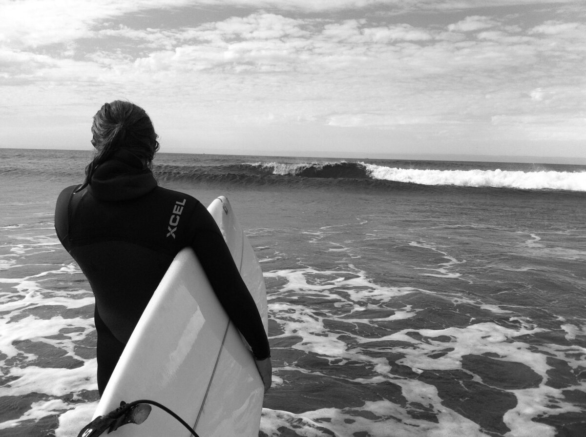Nicole holds surfboard while walking into the ocean in Iceland.