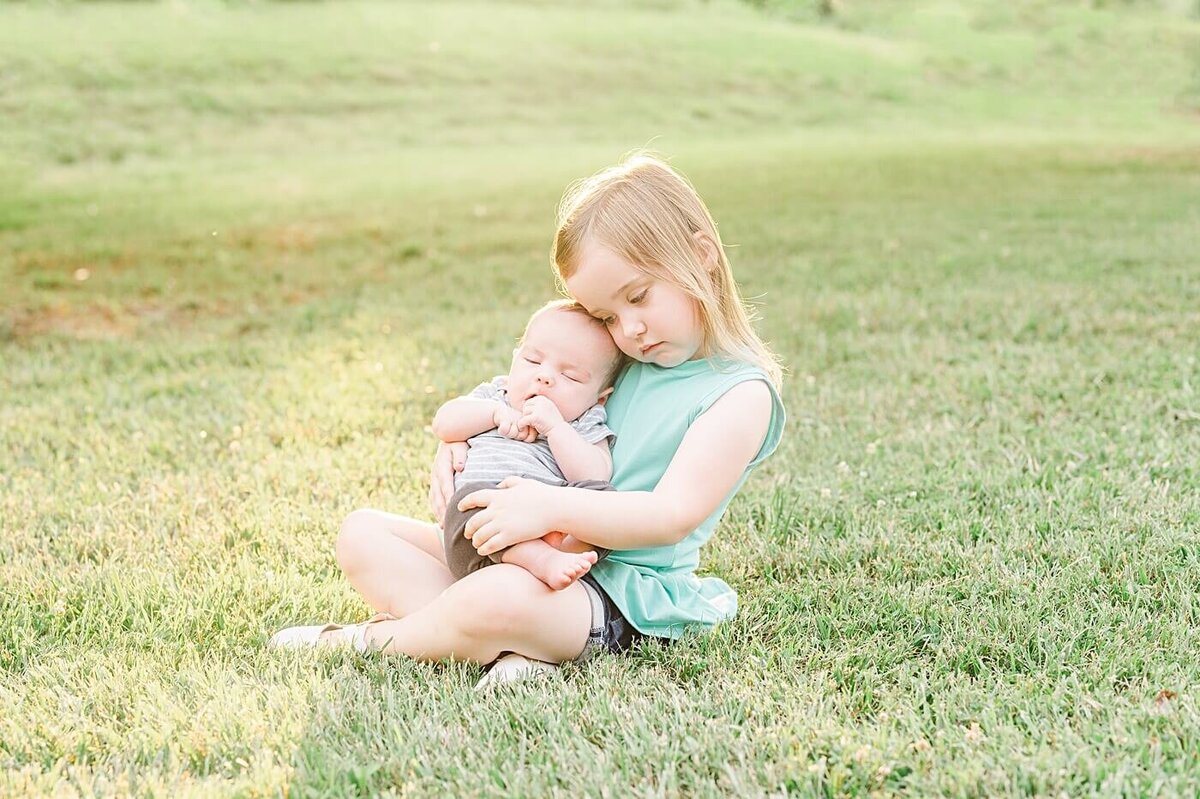 big sister holding baby brother in field at glenn hilton park in hickory nc family photosession