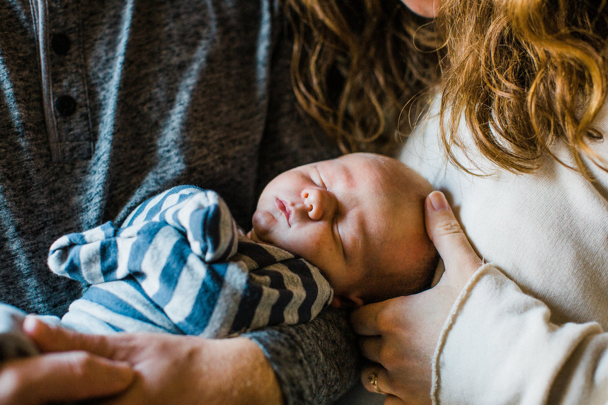 Close up family photo in Boone, NC of an infant behind cradled by his mother and father during a newborn family session.