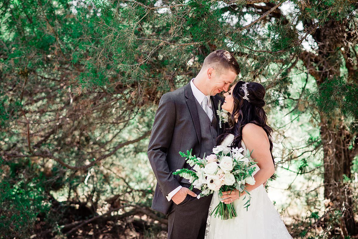 Bride and groom nose to nose  under a shaded tree on a bright sunny Montana day