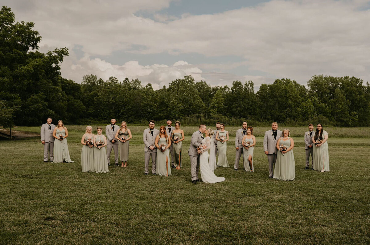 Wedding party in sage green dresses and gray suits in a field