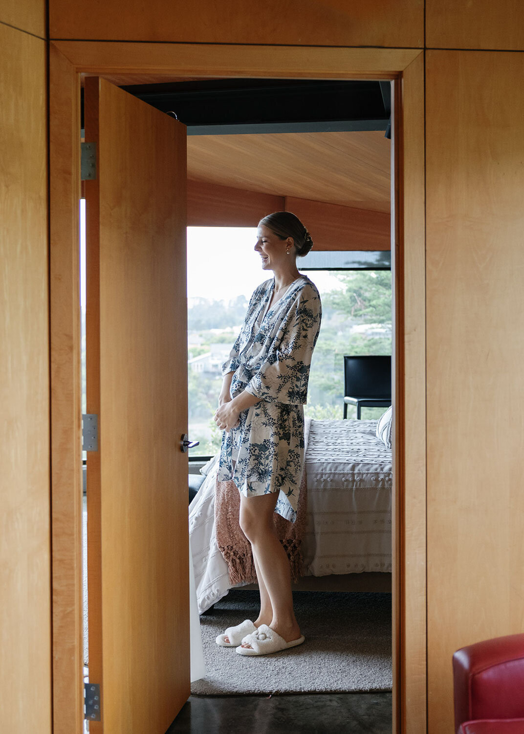 Bride in a floral robe standing in a wooden doorway smiling