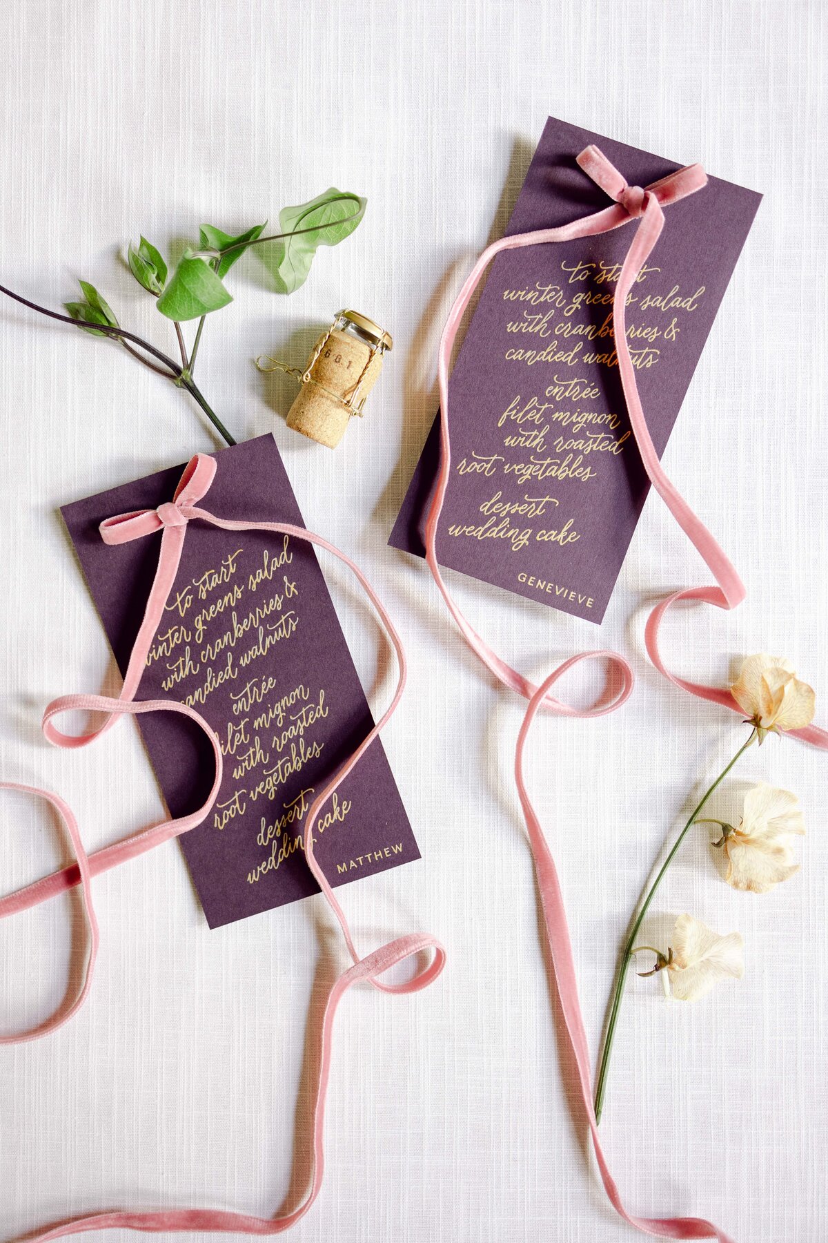 Flat lay shot of plum colored wedding dinner menu with florals and ribbon