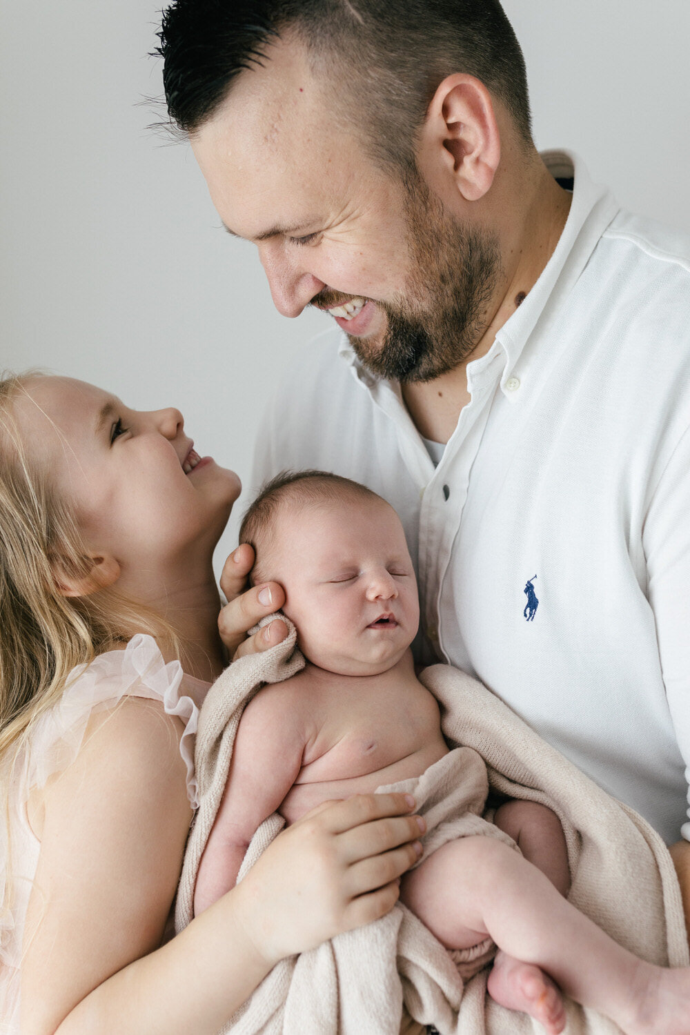 dad holds baby and daughter whilst they smile at eachother