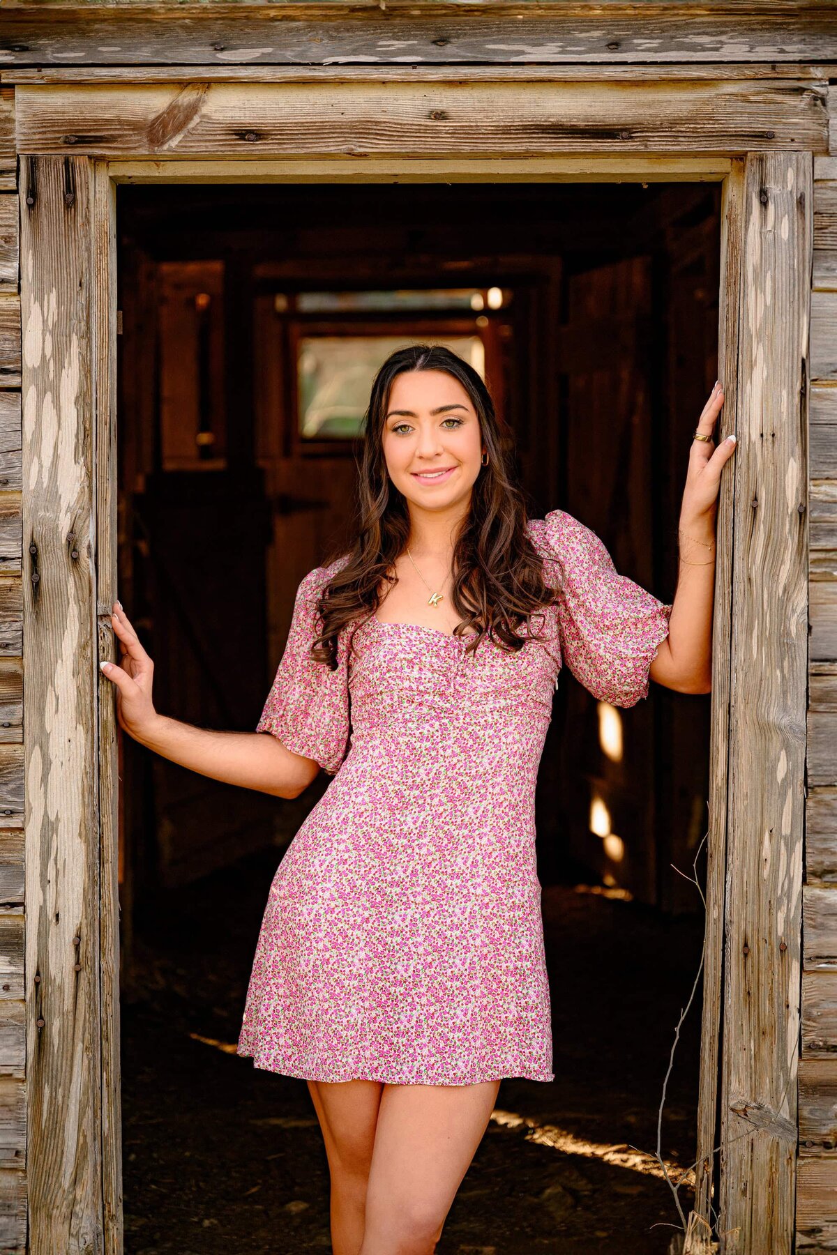 dark hair marvin ridge high school senior stands in a barn doorway wearing a flower dress