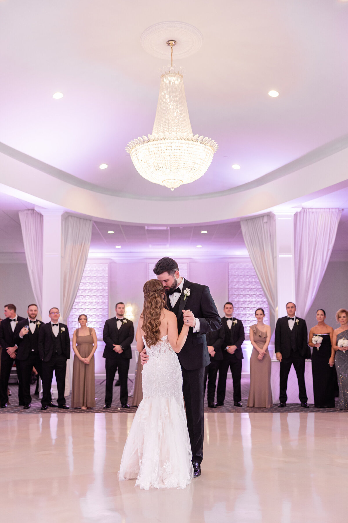 A newly wed couple shares their first dance as their friends and family surround them