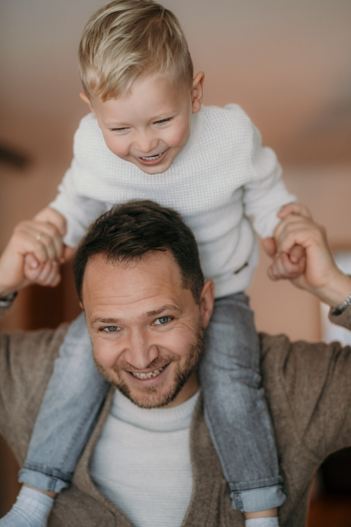 Father and son moment during family photography where the boy sits on dads shoulders - both laughing.