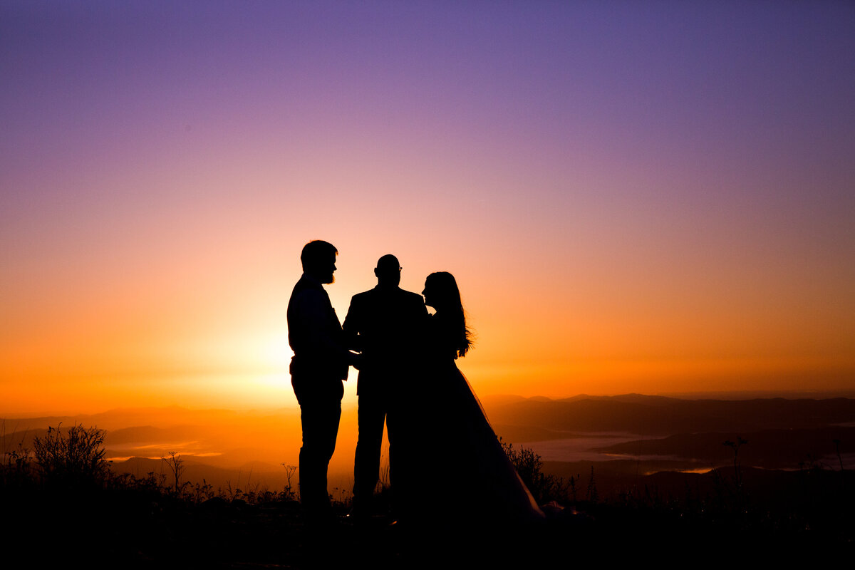 couple gets married by an officiant in the nc montains as the sunrise glows magically behind them 
