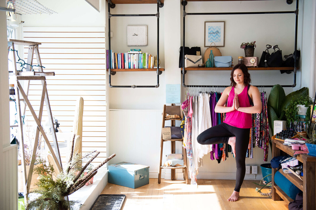 a yoga instructor with a pink tank and black tights demonstrates a standing pose in her studio.  Captured by Ottawa Branding Photographer JEMMAN Photography COMMERCIAL