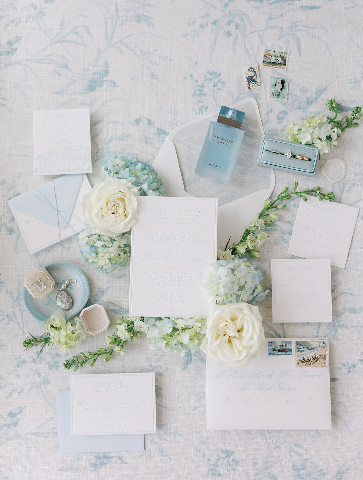 Wedding invitations sitting on a white background with blue flowers.