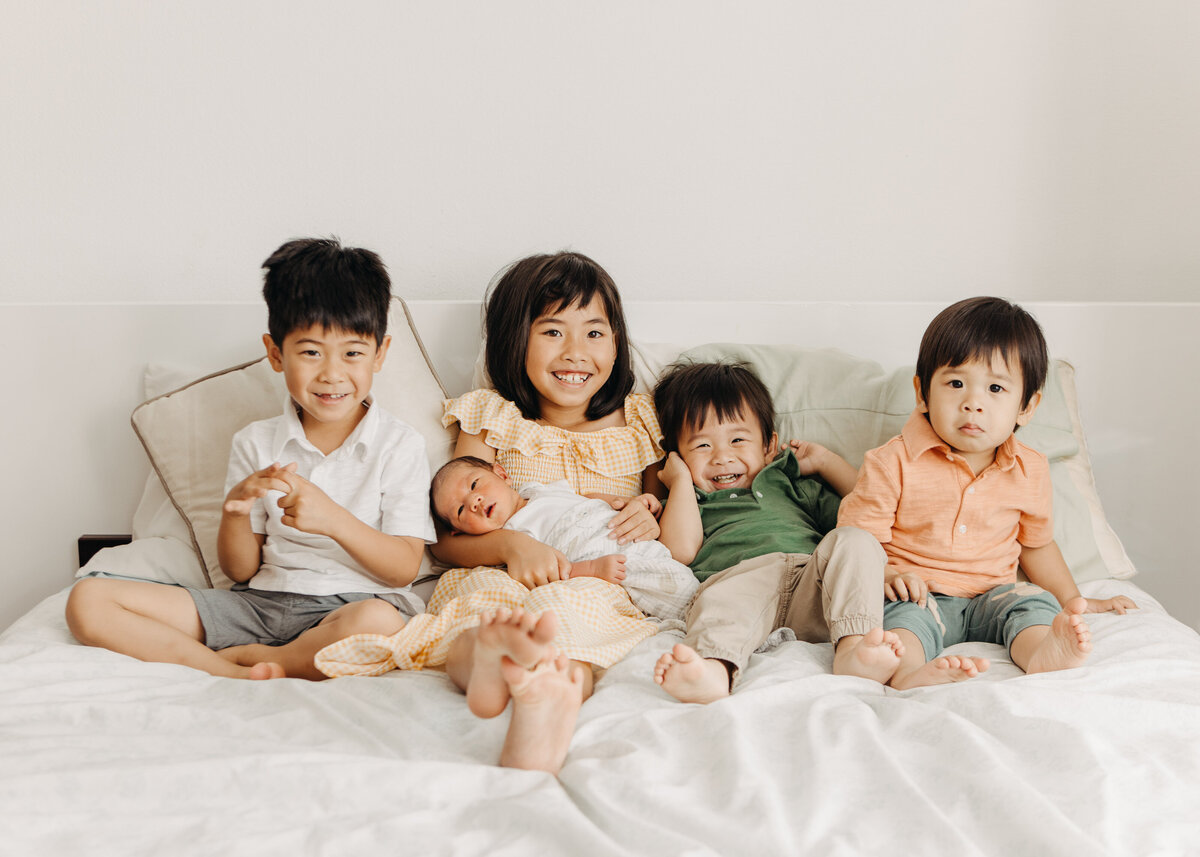 Family of five kids with newborn sibling on bed