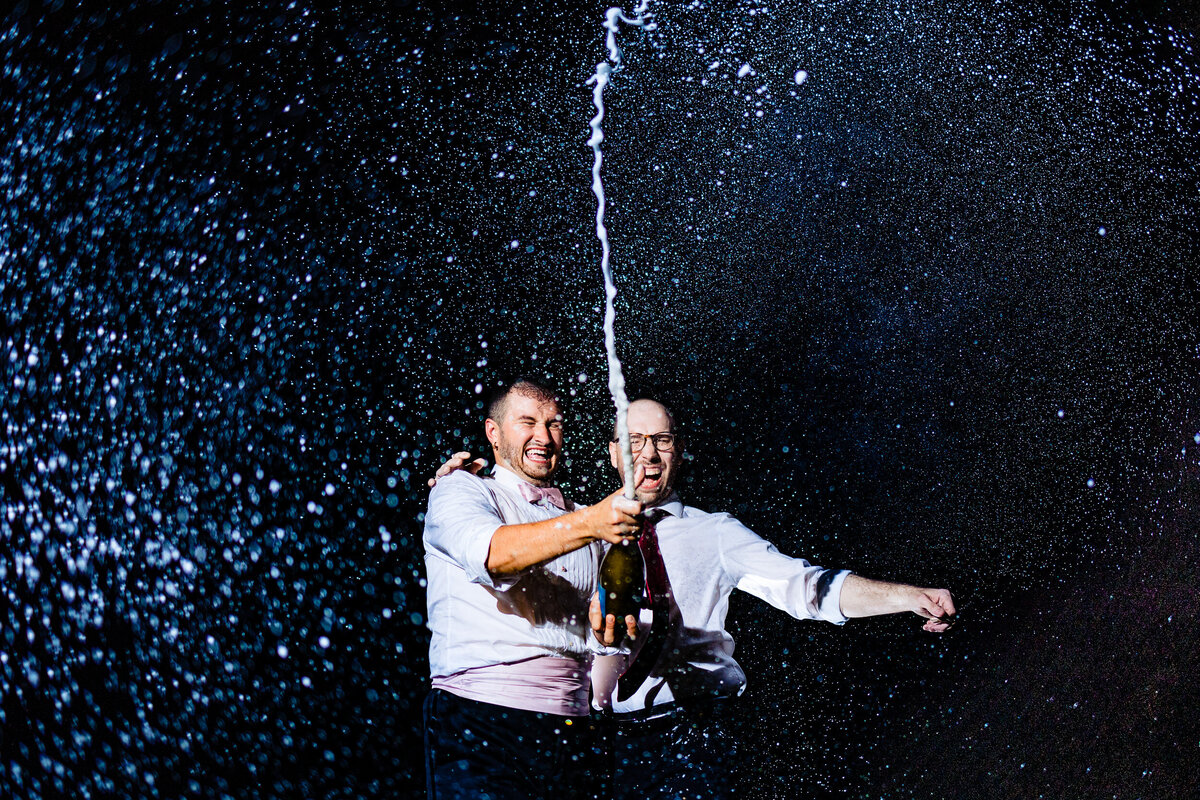 One of the top wedding photos of 2021. Taken by Adore Wedding Photography- Toledo, Ohio Wedding Photographers. This photo is of two grooms popping champagne at the  end of the night.