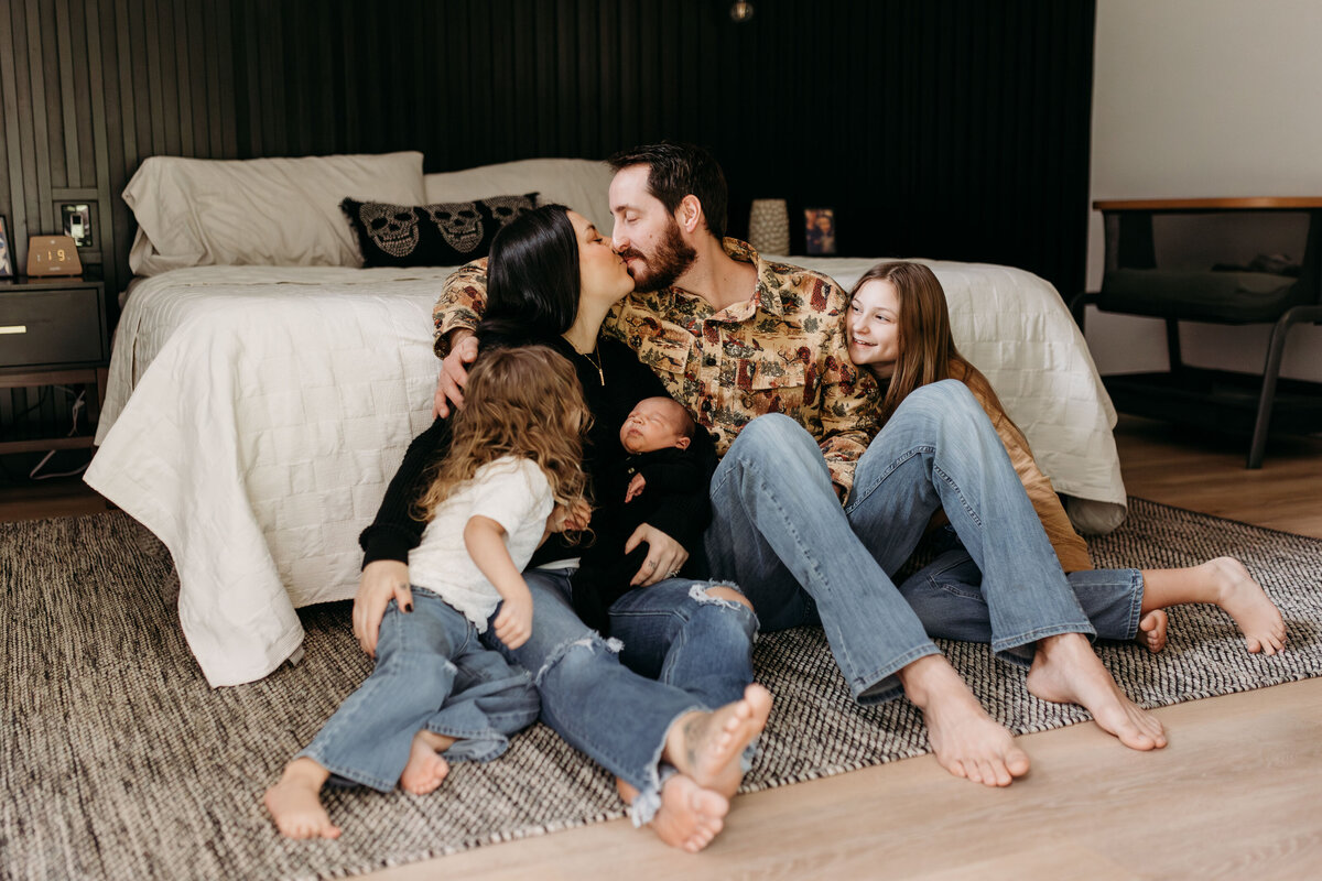 A family sits on the floor of their home, snuggling and admiring their newborn baby