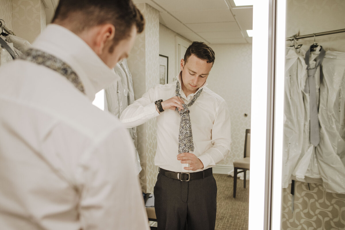 A man carefully adjusting his tie in the mirror as he prepares for a formal event taken by jen Jarmuzek photography a Minneapolis wedding photographer