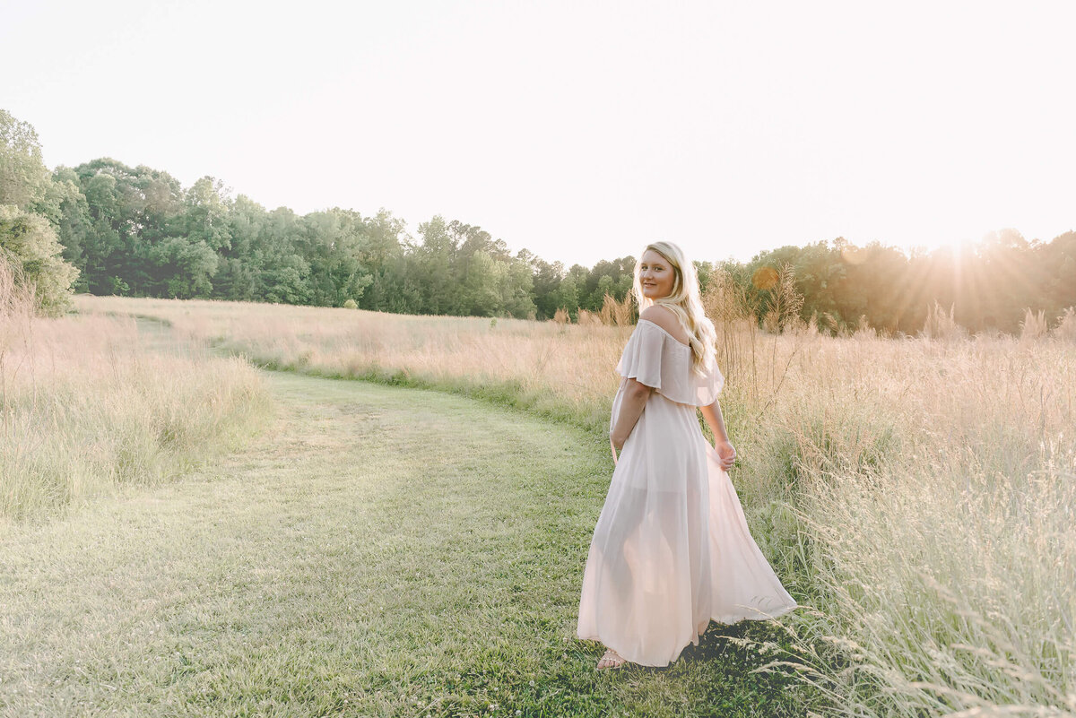 pregnant woman wearing a maternity gown in a field in raleigh nc